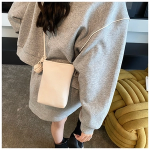 Detailed texture of cream crossbody phone bag with woven ball charm on grey hoodie