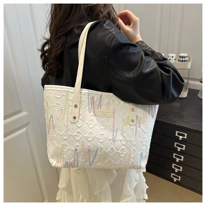 Dettaglio della borsa tote bianca trapuntata con ricami colorati e placca del marchio