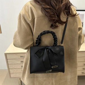 Sac bandoulière noir élégant avec grand nœud en satin et poignée tressée sur un buffet