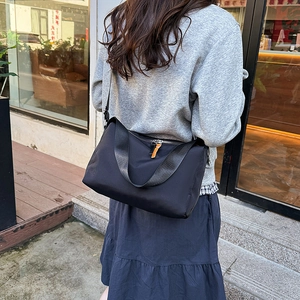 Minimalist black nylon crossbody messenger bag shown on model in a casual street setting