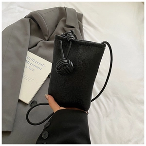 Close-up of black lychee leather mini bucket bag featuring large woven knot strap details