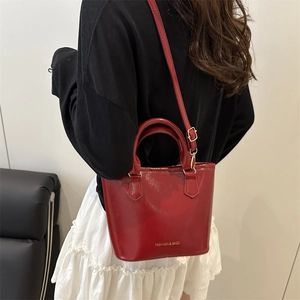 Red glossy bucket bag with top handles and adjustable strap shown on model back
