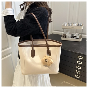 Model wearing a large cream leather tote bag with brown straps and a cute plush bear charm