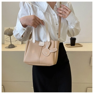 Detail of minimalist khaki bucket bag featuring white handles and a cute rabbit charm