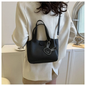 Detail of a black leather crossbody bag with a fashion logo and a cute bunny pendant charm