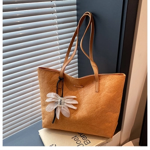Detail einer orangefarbenen strukturierten Tragetasche mit weißem Blumenanhänger