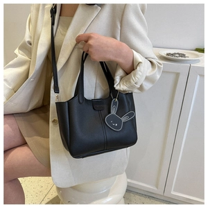 Detail of minimalist black leather bucket bag featuring a cute rabbit charm and shoulder strap