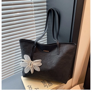 Detail der schwarzen Shopper Tasche mit Knitteroptik, Blumenanhänger und dünnen Trägern