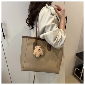 Detail of khaki tote bag with plush bear charm worn on a trench coat shoulder
