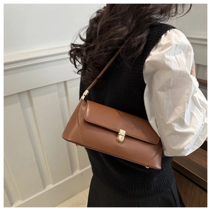 Close-up of a brown leather baguette bag with a gold buckle worn on the shoulder