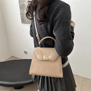 Elegant beige glossy trapezoid crossbody bag with gold hardware shown on a model