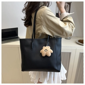 Close-up of black matte leather tote bag with a cute plush bear charm in an office setting