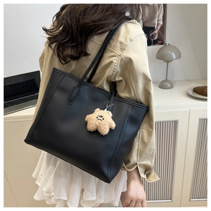 Side view of a large black leather tote bag with a cute plush star charm on a woman's shoulder