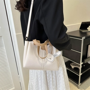 Minimalist beige bucket bag with brown handles and a cute rabbit charm on plain leather