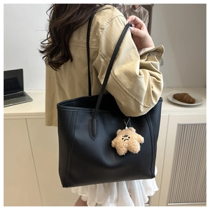 Minimalist black tote bag with plush star charm shown from side view on woman shoulder