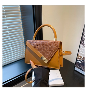 Detail of tan crocodile embossed texture on a handbag with golden twist lock hardware