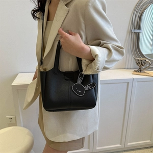 Minimalist black leather bucket bag with bunny charm and adjustable shoulder strap
