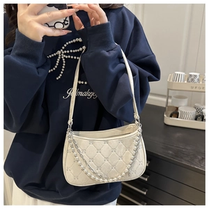 Close-up of beige quilted baguette bag with decorative pearl and silver metal chains