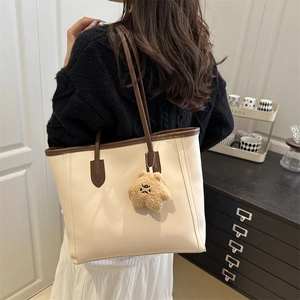 Minimalist beige tote bag with brown trim and bear charm shown on model shoulder
