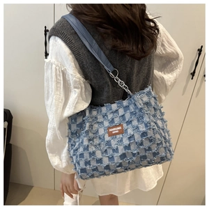Close-up of blue checkerboard denim bag featuring frayed edges and silver chain strap