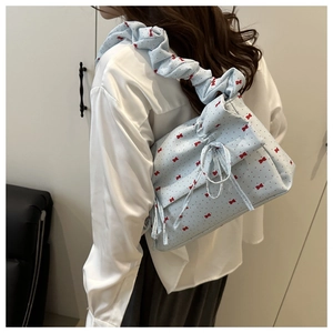 Close-up of light blue shoulder bag featuring red bow prints and ruffled strap detail