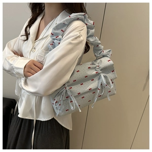 Detail of light blue shoulder bag with red bow prints and ruffled strap on model
