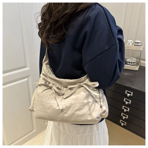 Close-up of beige nylon pleated shoulder bag with decorative ribbon bow and zipper detail