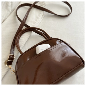 Detail showing deep brown glossy mini handbag with side pocket and white earbud case