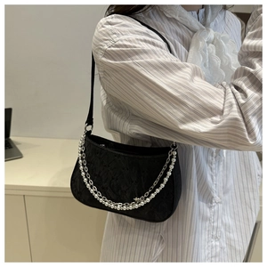 Detail of black textured hobo bag with silver chain and pearl strap on model's shoulder