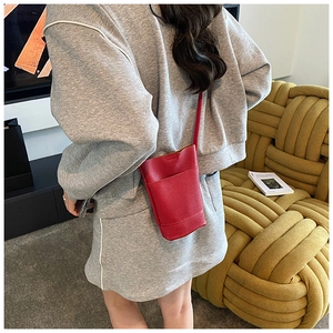 Close-up of a red litchi grain leather mini crossbody phone bag worn by a model