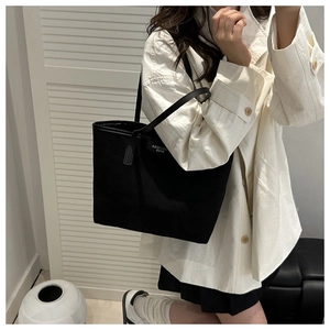 Detail of a minimalist black tote bag with brand label worn by model in a modern room