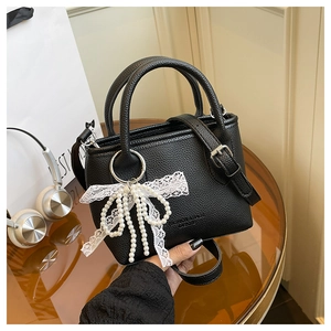 Détail du sac seau noir en cuir avec nœud en perles et pendentif en dentelle