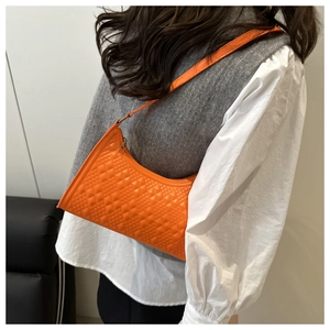 Side view of a bright orange quilted shoulder bag showing textured faux leather detail