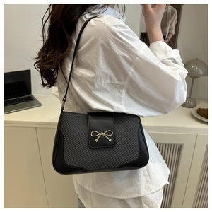 Détail du sac bandoulière noir à texture tissée avec un fermoir en nœud doré élégant