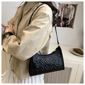 Detail of black underarm bag with geometric embossed texture and gold zipper hardware