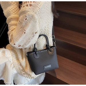 Detail of black woven bucket bag showing trapezoid shape and metallic fashion label