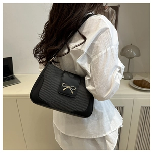 Détail du sac bandoulière texturé avec fermoir nœud doré sur le rabat en cuir noir