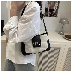 Détail du sac tissé contrasté avec fermoir nœud doré et bandoulière en cuir noir