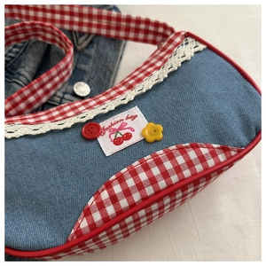 Dettaglio borsa a tracolla in denim blu e quadri rossi con pizzo e motivo ciliegia
