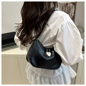Close-up of black leather shoulder bag featuring a white heart-shaped bow metal buckle