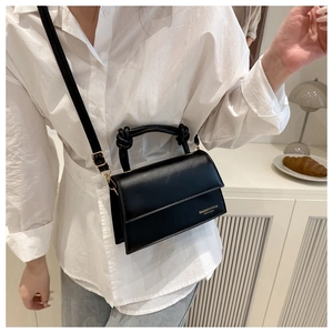 Detail of minimalist black handbag with knot handle and golden logo worn by model