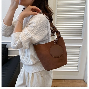 Détail d'un sac seau en daim marron foncé doté d'une bandoulière spirale tissée et d'un patch rond