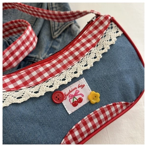 Dettaglio della borsa in denim con bordo a quadretti rossi, patch ciliegia e pizzo