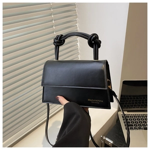 Close-up of black leather handbag featuring a knotted handle and gold printed logo detail