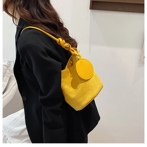 Detail of yellow suede bucket bag featuring a twisted handle knot and round charm detail