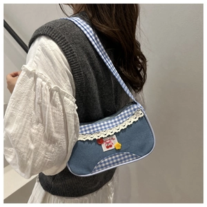 Dettaglio borsa a quadretti blu con bordo in pizzo, patch ciliegia e decoro floreale