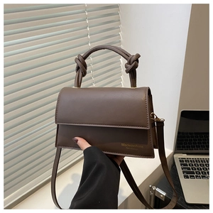 Close-up of brown textured leather handbag with creative knotted handle and flap design