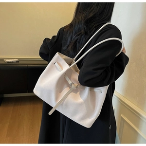 Detail of white woven texture tote bag featuring decorative buckle and slender strap