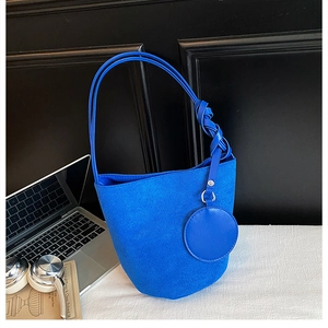 Klein blue suede bucket bag with round coin purse detail and knotted strap on a desk