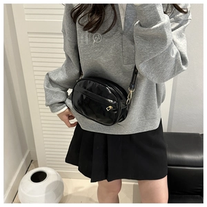 Glossy black patent leather crossbody bag with gold hardware shown on a model